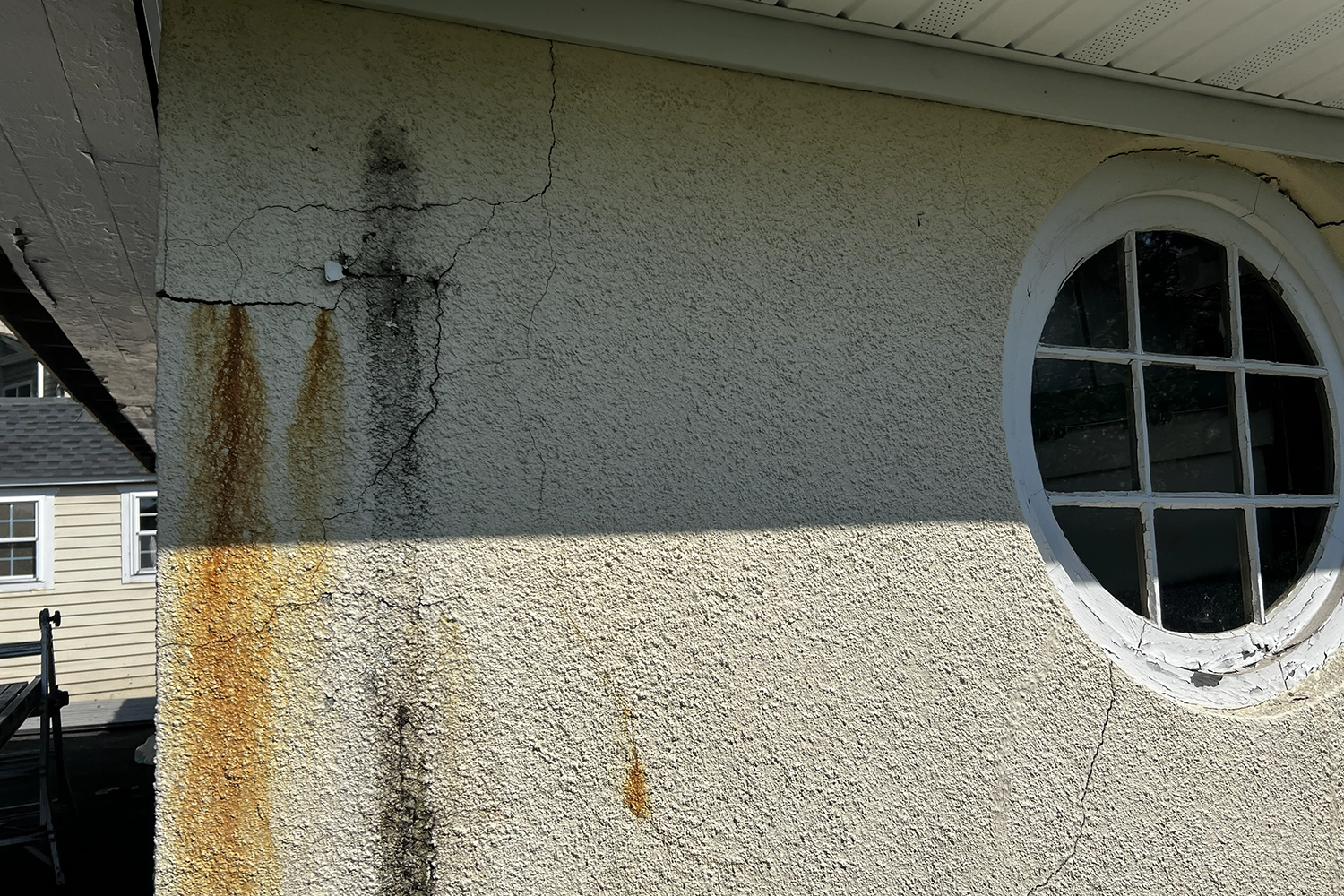 Stucco water damage with visible rust stains, mold growth, and vertical cracks indicating water intrusion and moisture damage requiring emergency repair