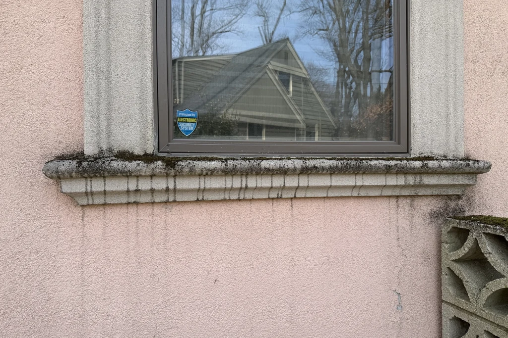 Stucco Leaking When It Rains? Causes & Emergency Fixes NJ 4 Water seepage and dark staining around stucco window sill with mold growth, showing failed window flashing and sealant failure causing water intrusion
