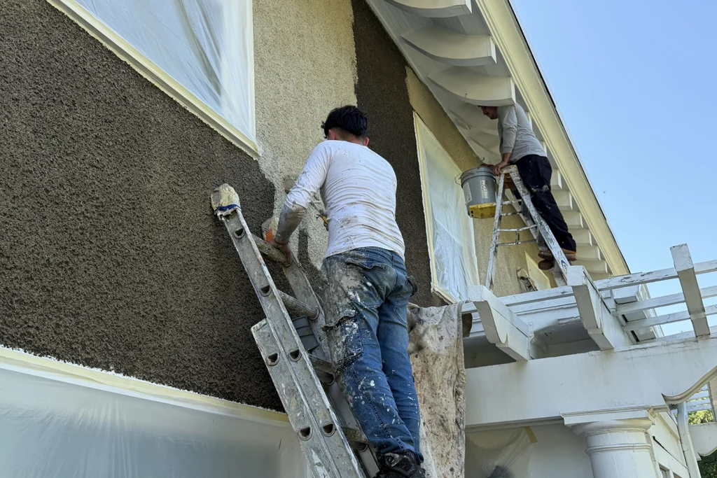 Stucco contractors applying a dark finish coat around windows on a residential exterior