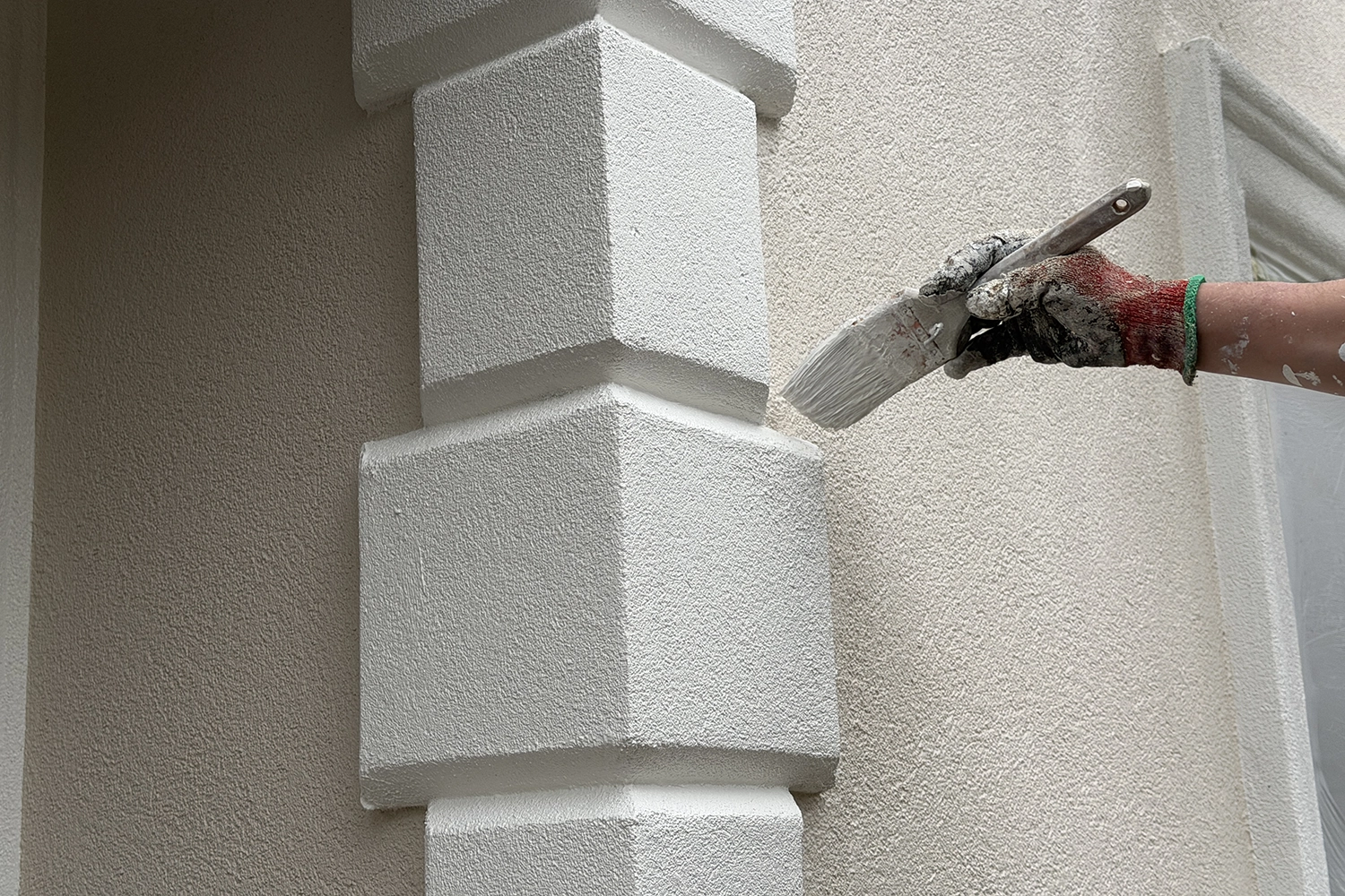 Contractor applying a fresh protective coating to decorative stucco trim to help prevent fading and weather damage.