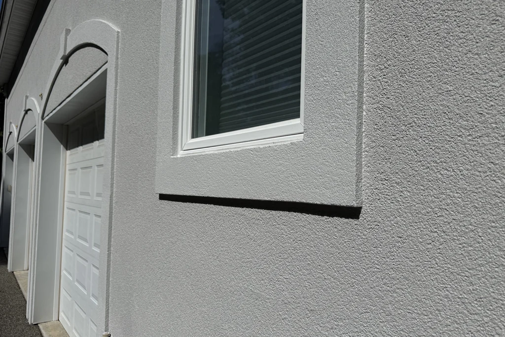 Close-up of a freshly coated stucco exterior with clean window trim and an even texture