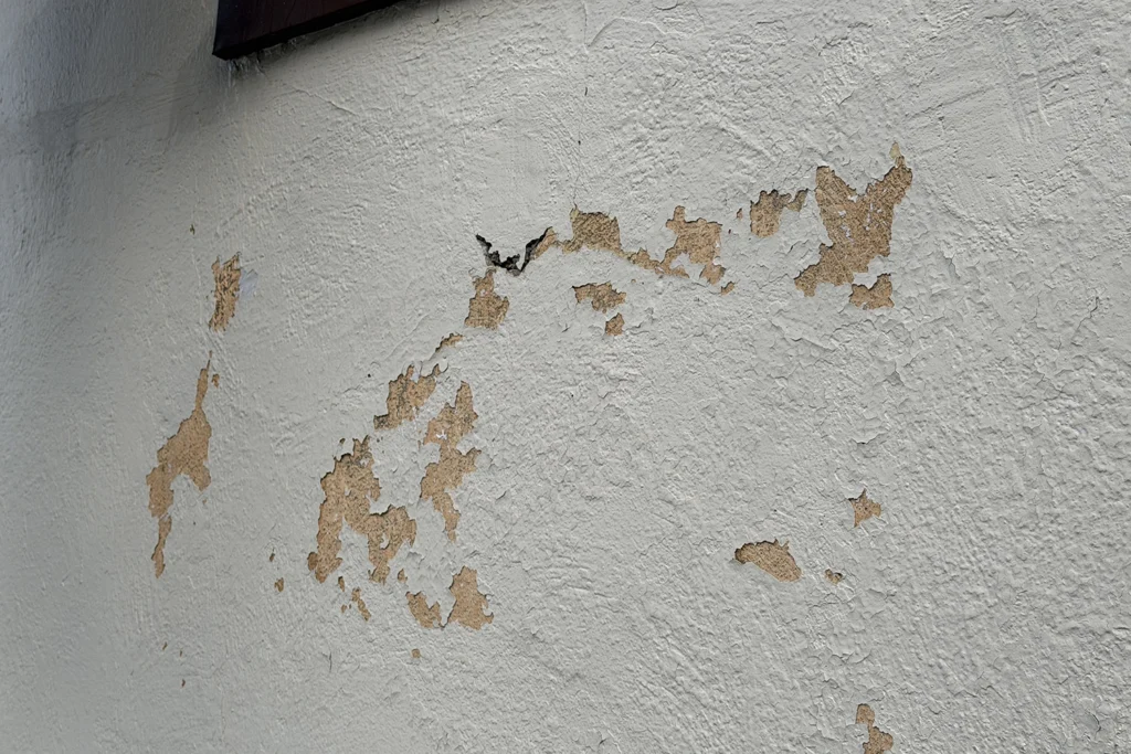 Stucco Repair vs Repainting: What Does Your New Jersey Home Need? 3 Close-up of peeling and flaking paint on an exterior stucco wall before repair