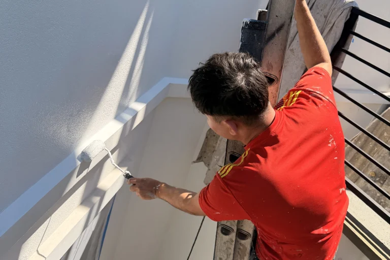 Contractor applying fresh exterior paint to a prepared stucco wall with a roller