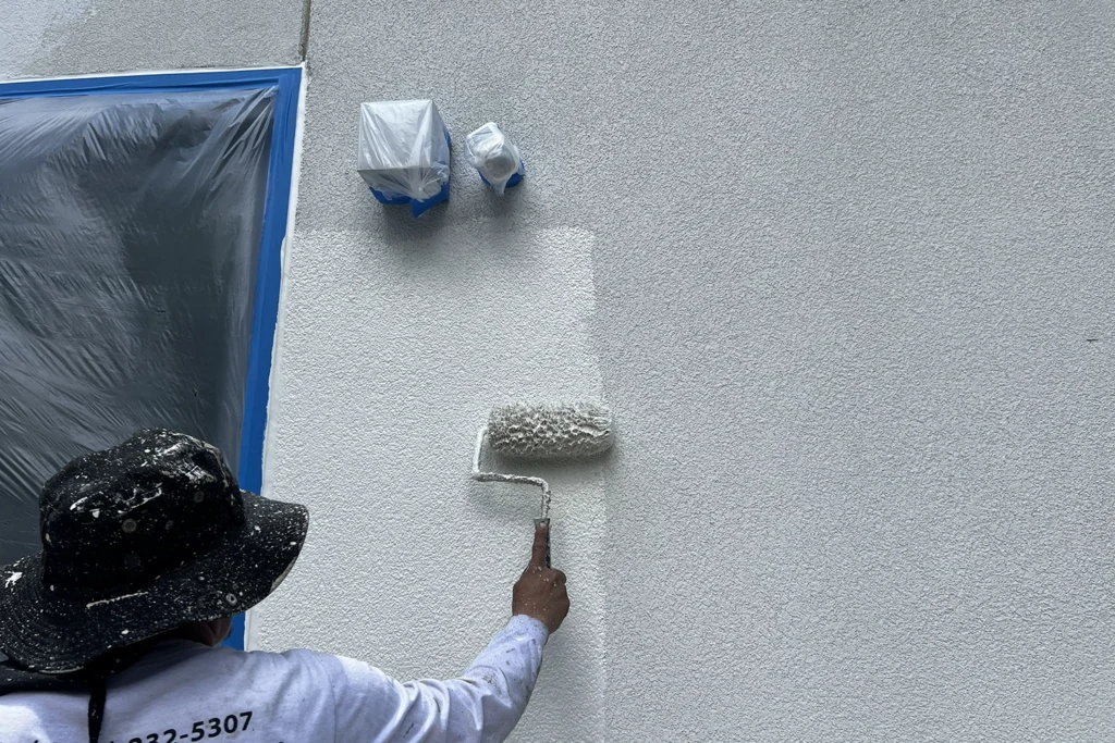 Contractor using a roller to apply a fresh white coating to a textured stucco wall