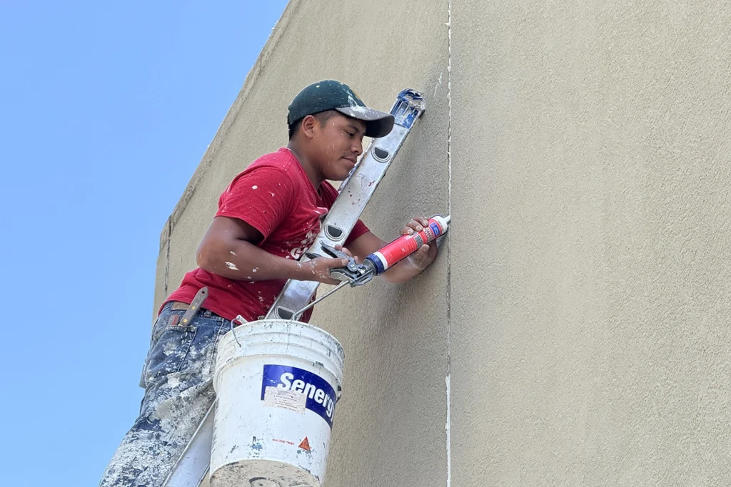 Contractor applying sealant to a vertical stucco joint before exterior coating work