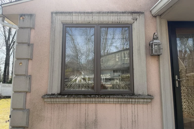 Pink stucco wall with dark water streaks and staining around the window frame and sill