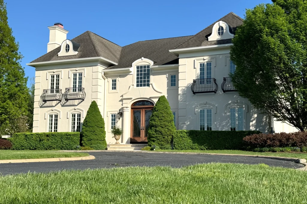 Angled view of the restored front stucco exterior and main entrance of a luxury mansion in Mendham, New Jersey.