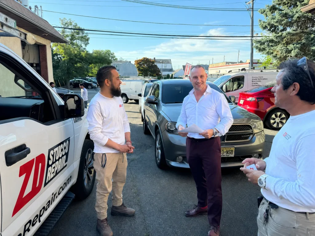 ZD Stucco Repair team discussing a stucco restoration project beside company vehicles