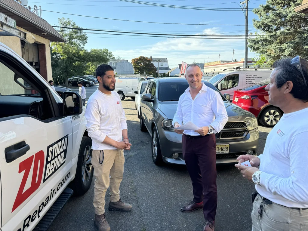 ZD Stucco Repair team discussing project details beside a branded company vehicle.