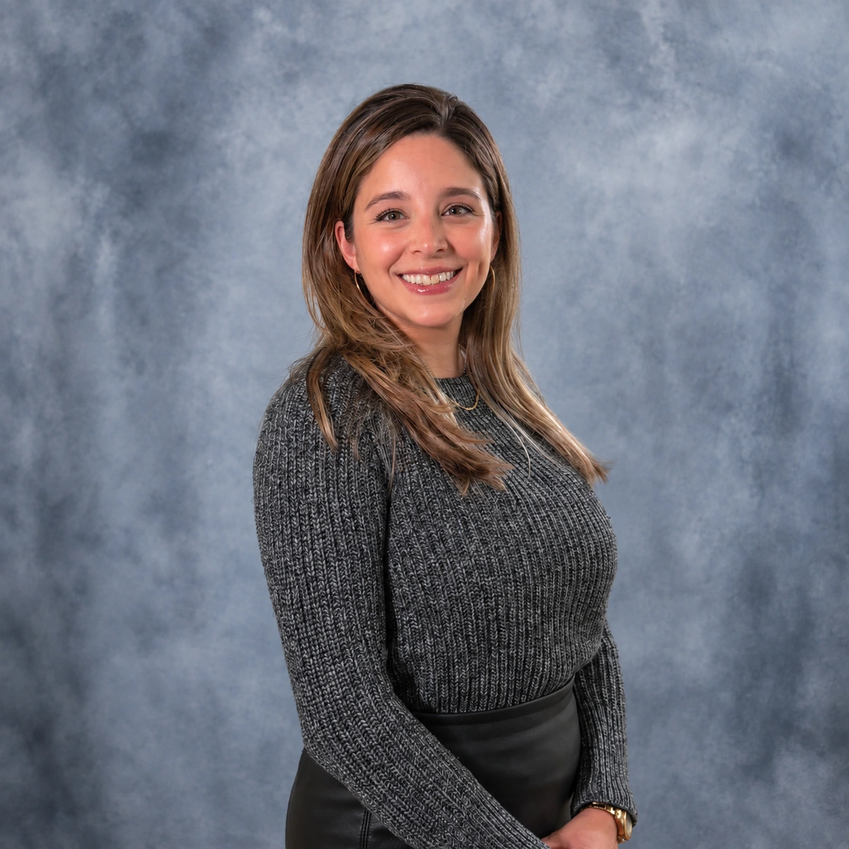Cristina Guzman, Finance Manager at ZD Stucco Repair, smiling in a gray sweater against a gray studio backdrop.
