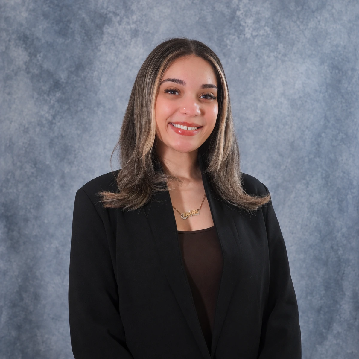 Sheila Chalas, Client Relations Coordinator at ZD Stucco Repair, smiling in a black blazer against a gray studio backdrop.
